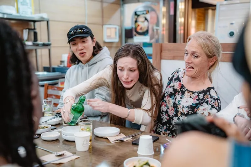 Small group eating tteokbokki and skewers with a host at a lively market stall on a seoul food tours street-food walk in Seoul, South Korea